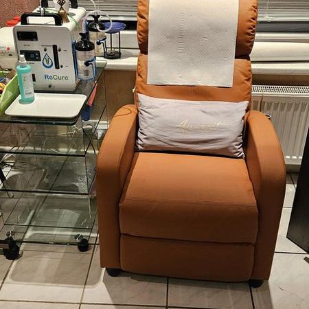Brauner Sessel mit Kopf- und Rückenkissen, daneben ein Rollwagen mit medizinischem Gerät.