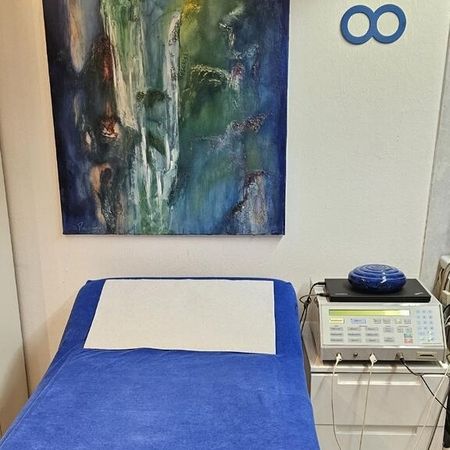 Behandlungsraum mit blauer Liege, Wandbild und medizinischem Gerät.