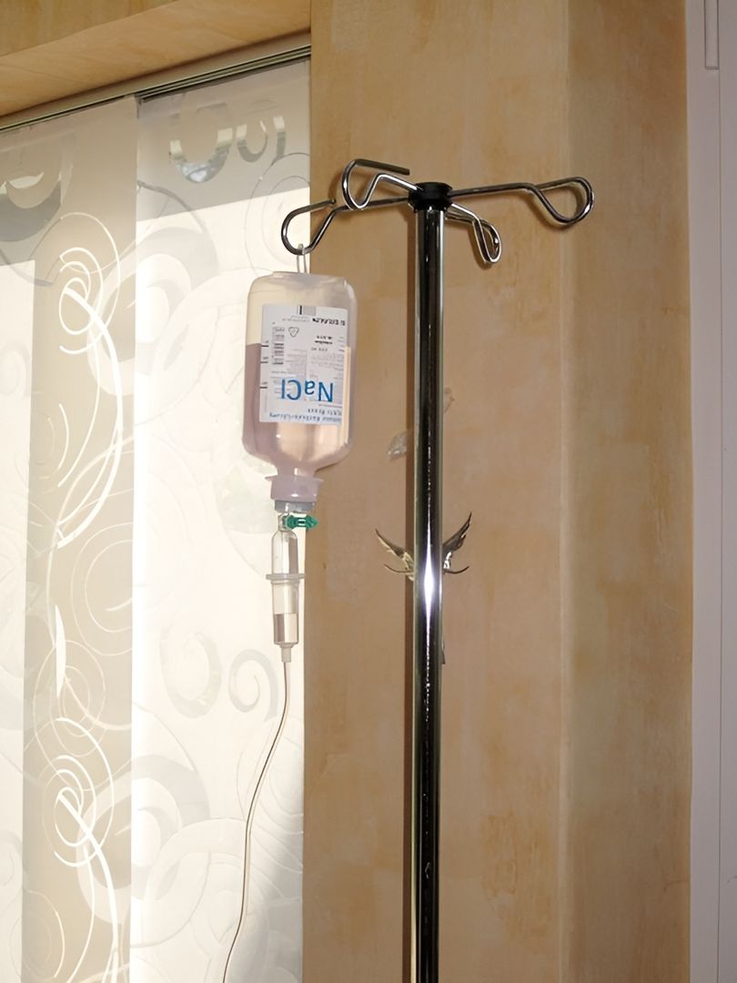 Infusionsflasche mit Natriumchlorid an Edelstahl-Infusionsständer vor heller Wand - medizinische Ausstattung für Infusionsbehandlungen im Therapiezentrum