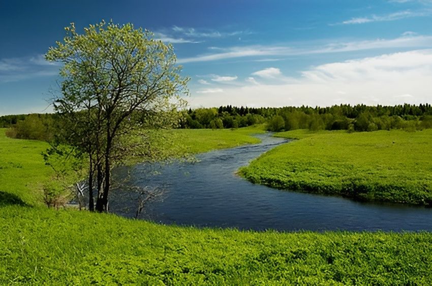 Landschaft mit grünem Tal und geschwungenem Fluss unter blauem Himmel - natürliche Idylle mit ruhiger Atmosphäre und frischem Frühlingsgrün